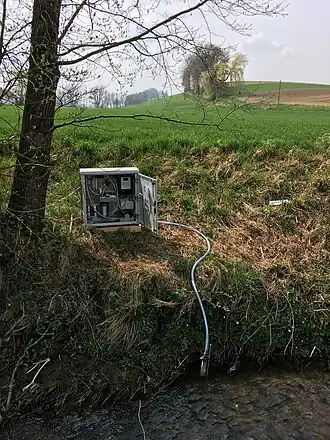 Das Foto zeigt einen automatischen Probenehmer, der an der Böschungskante eines Kleingewässers installiert ist