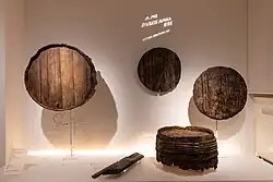 Verschiedene Fragmente von Holzfässern wie Böden, Deckel oder komplett erhaltene Fässer mit eingravierten Hinweisen wie Strichen für aufgeschriebene Schulden.