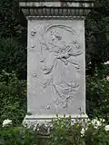 Das Postamentrelief von Wilhelm Rösch zeigt Euterpe, die Muse der Dichtkunst, mit Blumen und Kithara.