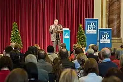 Heiko Ernst 2013 als Redner vor Publikum und dunkelrotem Bühnenvorhang auf der Fachtagung über "Glück und Seligkeit" im Palais Liechtenstein