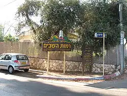 In die Siedlung führende seitlich bebaute Straße mit „Ortseingangsschild“.