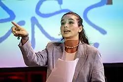 Schwarzhaarige Frau in einem grauen Jackett zeigt mit dem Finger auf einen Bildschirm