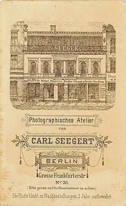 Revers CdV, Abbildung der Fensterfront des Ateliers (oberste Etage); davor Gitter mit Schriftzug „C. Seegert“; Atelier Carl Seegert, Berlin, Grosse Frankfurter Straße; Lithograf unbekannt; um 1880.