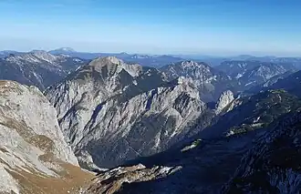 Blick über das Brunntal auf die Südwestseite der Riegerin mit der „Rothmäuer, “ darüber die bewaldeten Hochfläche der Riegerin-Alm. Der felsige Spitz gleich rechts unterhalb des Riegerin-Gipfels ist der Große Schober, der steil aufragende Abbruch am rechten (südlichen) Ende der Riegerin-Alm der Schönberg. Im rechten Bilddrittel der freistehende „Turm.“