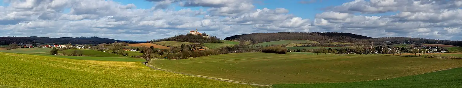 Landschaftsbild bei Altwiedermus (links) und Neuwiedermuß (rechts) mit der Burg Ronneburg links der Bildmitte. Rechts der Burg der Steinkopf im Ronneburger Wald. Hinter Altwiedermus Teile des Marköbeler Bergrückens.