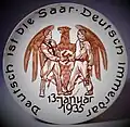 Gedenkteller mit Reichsadler mit Hakenkreuzemblem, davor reichen sich ein NS-Parteigenosse (links) und ein Saarbergmann mit Grubenlampe (rechts) die Hand, mit umlaufenden Slogan „Deutsch ist die Saar, deutsch immerdar“