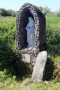 Antiker Kreuzstein mit Swastika neben einer modernen Ädikula-Heiligenfigur am katholischen Wallfahrtsort der St.-Brigid-Quelle bei Cliffoney, County Sligo in Irland