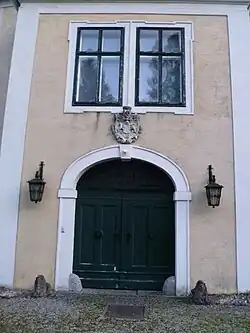 Frontalansicht des Torbaus mit einem korbbogigen Tor, darüber ein steinernes Wappenrelief und ein gekuppeltes Fenster