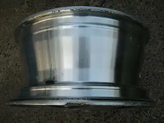 PKW-Felge mit Tiefbett und sichtbarem Autoventil. Felgenhörner mit Gummi-Abrieb. Am äußeren Felgenhorn ist eine Beschädigung erkennbar.