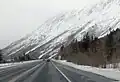 Winterliche Ansicht des Highways bei Kilometer 156 (Meile 97), Blickrichtung Norden, im Hintergrund die Chugach Mountains, links der Straße die Schienen der Alaska Railroad