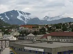 Foto einer Ortschaft, dahinter erhebt sich ein teils Schnee bedeckter Berg