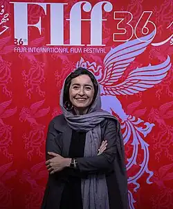 33-jährige Frau von prunkvoll gestaltetem Plakat des Fajr-Festivals, stehend mit verschränkten Armen, Kopftuch tragend, freundlich lächelnd