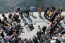 Blick von oben auf die Verlegung, eine Menschenmenge bildet einen Kreis um den Künstler, der am Boden vor den Steinen kniet.