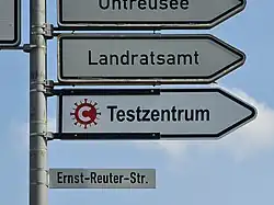 Das Foto zeigt ein richtungsweisendes Verkehrszeichen mit COVID-19-Symbol und Text „Testzentrum“