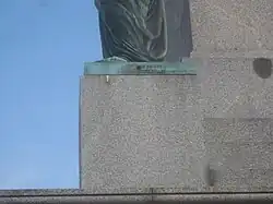 Bezeichnung an der Plinthe einer Statue.