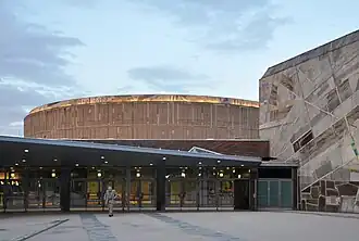 Hinten die konvexe Außenmauer des Beethoven-Saals. Davor eine Fassade mit abstraktem Mosaikbild, darunter der Eingangsbereich. Rechts der Mozart-Saal.