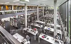 Großer Lesesaal der TIB mit modernen Arbeitsplätzen, hohen Bücherregalen und viel Tageslicht durch bodentiefe Fenster