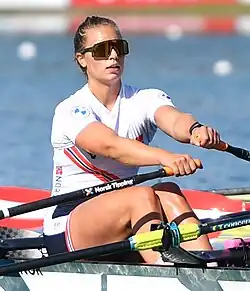 Helseth rudert im Doppelzweier. Sie trägt eine blaue Hose, ein weißes Trikot mit rot-blauem Streifen und eine Sonnenbrille.