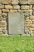 In die Außenmauer eingelassenes verwittertes Epitaph mit Rollwerk verziert