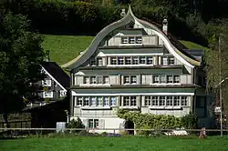 Fabrikanten- und Handelshaus mit Schweifgiebeldach aus dem Jahr 1813, Eingang mit Rundbogenportal und über Ost- und Westseite durch­laufendem Klebdach in Spreitenbach, Brunnadern[6][51]