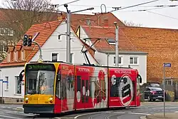 Dreiteiliger Straßenbahnwagen mit roter Vollwerbung. In der Zielanzeige steht in grüner Schrift „5 Nordhausen Ost“.