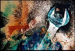 Farbaufnahme mit verschiedenen Farbspritzern und Farbmustern. Im rechten Bereich dominieren Schwarz und Dunkelblau, in dessen Mitte ein blauweißer Maulschlüssel ist.