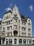 Trier, Porta-Nigra-Platz 5: repräsentatives viergeschossiges Eckwohn- und Geschäftshaus, historisierender Putzbau, bezeichnet 1905, Architekten Julius Wirtz und Wilhelm Schmitz