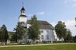 Foto einer weißen Holzkirche, im Vordergrund ein Friedhof