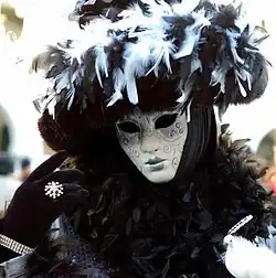 Eine Person beim Karneval in Venedig in einer traditionellen venezianischer Verkleidung für Frauen mit Gesichtsmaske und einer farblichen Komposition in Silber und Schwarz