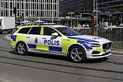 Das Bild zeigt einen modernen Kombi-PKW der Marke Volvo mit eingeschaltetem Blaulicht, Markierungen und Beschriftung der schwedischen Polizei.