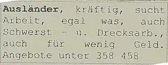 Eine Zeitungsannonce auf vergilbtem Papier ist zu sehen, in fünf schmalen Zeilen formatiert und mit grauem Rahmen, in Schreibmaschinenschrift gedruckt, teils mit Abkürzungen. Darauf steht: „Ausländer, kräftig, sucht Arbeit, egal was, auch Schwerst – u. Drecksarb., auch für wenig Geld. Angebote unter 358 458“. Das erste Wort „Ausländer“ ist fett gedruckt.