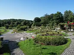 Ein halbrund an einem leichten Hang angelegter Rosengarten, im Vordergrund ein Brunnen