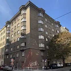 Frontalaufnahme des Eckhauses mit 6 Stockwerken und Erkerfenstern unter blauem Himmel