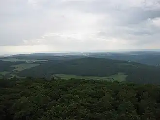 Blick vom Aussichtsturm Pferdskopf zum Wolfsküppel (mittig) im Östlichen Hintertaunus – mit Dorf Riedelbach (links)