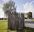 Blick aus dem Barbaricum: vorn die nachgebaute Limespalisade, rechts der rekonstruierte Holzturm, hinter der Palisade die originäre Holzturmstelle