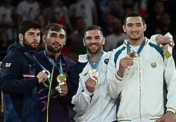 Vier Medaillengewinner zeigen ihre Medaille, die beiden links tragen eine blaue Trainingsjacke, die beiden rechts eine weiße Trainingsjacke