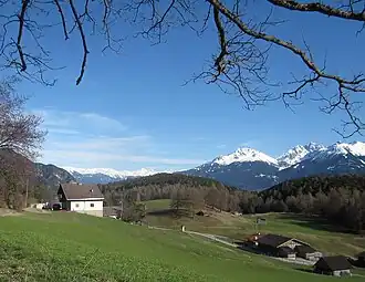 Blick vom Seefelder Plateau nach Südosten zum bewaldeten Zirler Berg (mittig); davor zwischen den Häusern die Pestsäule von Leithen; hinten rechts die Marchreisenspitze, links daneben die Saile; links daneben am Horizont die Tuxer Alpen