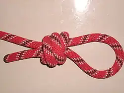 Der Zweistrang-Bändselknoten mit dreifachem Überhandknoten. Die Törns werden in entgegengesetzter Richtung wie beim Henkersknoten gewickelt und das Arbeitsende läuft innen durch die Törns zurück.