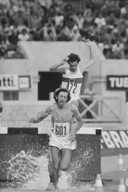 Schwarzweißfoto, auf dem Fava nach dem Wassergraben wieder Fahrt aufnimmt. Er trägt das blaue italienische Nationaltrikot und eine weiße Hose. Im Hintergrund sieht man den Deutschen Michael Karst bei der Überquerung des Wassergrabens.